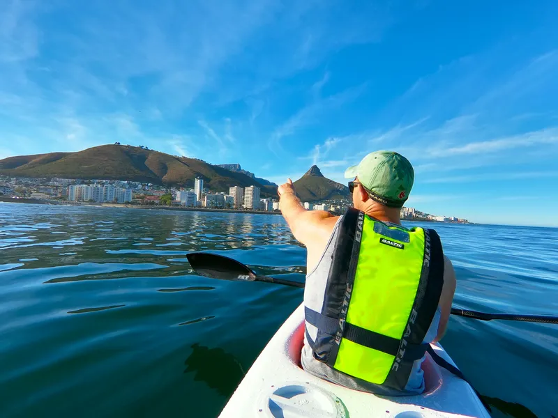 A guide in a kayak pointing towards Lion’s Head, with Signal Hill and the Sea Point shoreline behind